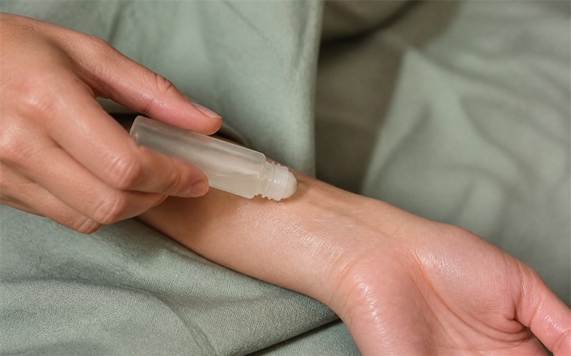 A close natural view of an unbranded roll-on perfume gliding across a wrist, leaving a subtle clear sheen; only a small believable skin area is visible