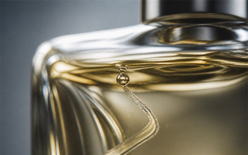 A macro view of a pale amber fragrance liquid gently rotating inside an unbranded clear bottle as a small air bubble rises, showing gradual change and oxidation without labels or text
